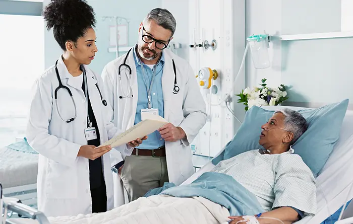 Two doctors next to the patient lying on his bed in the clinic ward